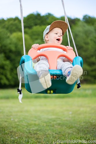 Image of Adorable little happy Caucasian infant baby boy child swinging on playground outdoors.