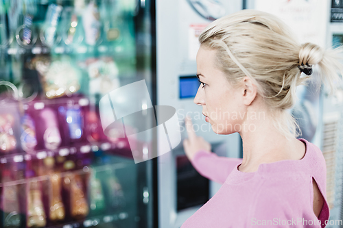 Image of Caucasian woman using a modern vending machine. Her right hand is placed on the dia pad