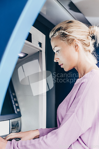 Image of Young lady withdrawing money at ATM machine entering her pin code.