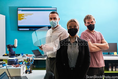 Image of A group of colleagues stand ingin a robotics laboratory, arms crossed, wearing protective masks, symbolizing their teamwork and commitment to technological innovation and scientific research.