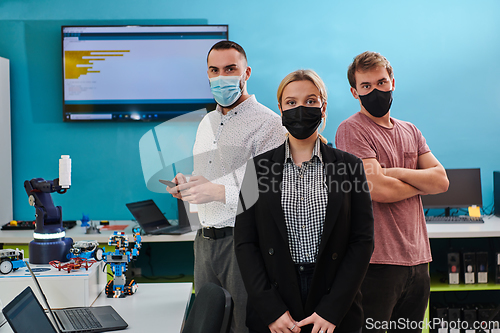 Image of A group of colleagues stand ingin a robotics laboratory, arms crossed, wearing protective masks, symbolizing their teamwork and commitment to technological innovation and scientific research.