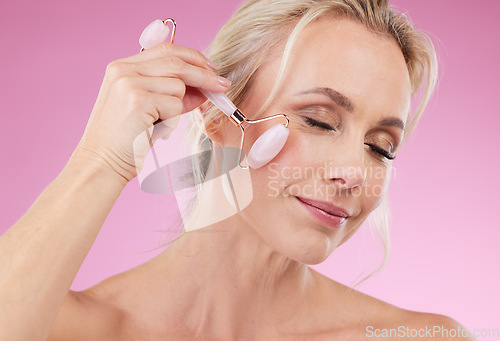 Image of Face roller, beauty and woman facial massage with dermatology and cosmetic tools. Happy mature person on pink background for skincare, self care and rose quartz results for anti aging, glow and shine