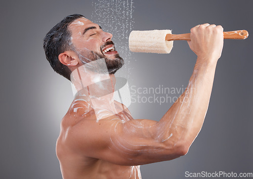 Image of Shower, cleaning and man singing with brush in studio for skincare, washing body and wellness on gray background. Beauty, bathroom and happy male do karaoke with loofah sponge, soap and water splash