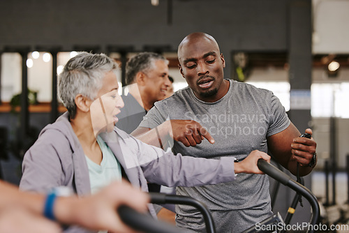 Image of Elderly group, exercise bike and personal trainer for fitness, timer and retirement wellness by blurred background. Senior woman, bicycle training and diversity with black man, progress and coaching