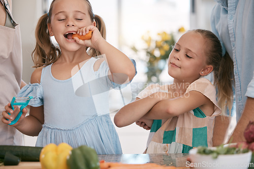 Image of Children, cooking and a girl eating a carrot in the kitchen while preparing a healthy meal with her family. Kids, food and nutrition with a female child sister biting a vegetable in her home