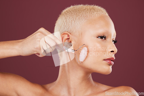 Image of Face skincare, jade roller and woman in studio isolated on a red background for dermatology. Beauty, cosmetics and female model with product or rose quartz stone for facial treatment and healthy skin