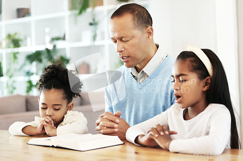 Image of Family, worship and bible with father and kids praying at table for peace, religion and faith in their home. God, pray and children with parent for prayer, bible study or Jesus Christ praise together