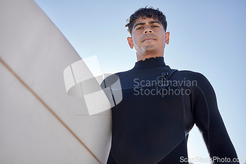 Image of Surfing, beach and serious surfer with blue sky outdoor for water sports, training and exercise. Surfboard, morning workout and sea with summer sun and man ready for sport and freedom at the ocean