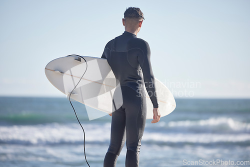 Image of Back, surfing man and standing at beach with board, freedom and summer waves with blue sky. Surfer guy at sea, sunshine and travel for water sports, adventure and ocean in nature