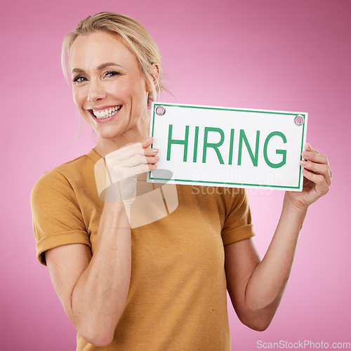 Image of Hiring, sign and portrait of a woman for recruitment, job search and advertising opportunity. Smile of a happy business person with a poster for recruiting and human resources on a pink background