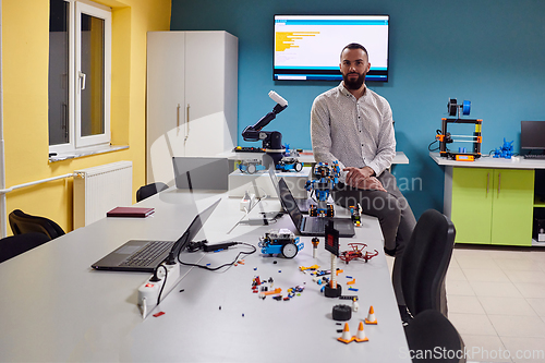 Image of A bearded man in a modern robotics laboratory, immersed in research and surrounded by advanced technology and equipment.