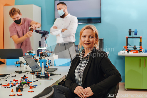 Image of A woman sitting in a laboratory while her colleagues test a new robotic invention in the background