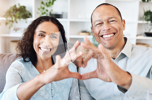 Image of Hand, heart and portrait of mature couple with love on sofa for bond, romance and happy in living room. Hands, emoji and face of older man with woman, happy or smile while enjoying retirement at home