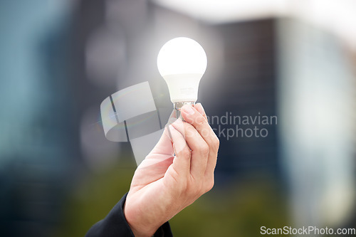 Image of Hands, light bulb and idea in the city for solution, eco friendly or renewable energy on blurred background. Hand of person holding lamp for creativity, ideas or power saving element on mockup