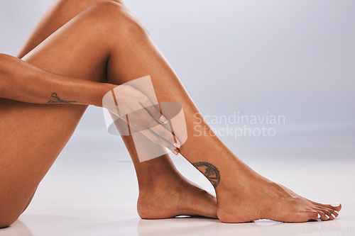 Image of Hand, legs and body with a black woman in studio, sitting on the floor against a gray background for skincare. Fitness, beauty and tattoo with a female posing alone for hair removal, laser or wax