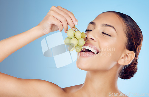 Image of Skincare, grapes and woman in studio for wellness, detox or organic treatment on blue background. Fruit, snack and girl model with relax during beauty, routine and happy with raw product isolated