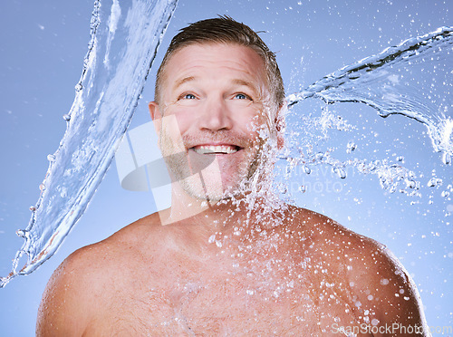 Image of Showering, water splash and man with smile, cleaning and daily hygiene on blue studio background. Mature male, gentleman and clear liquid for washing, dermatology and skincare for grooming on backdro