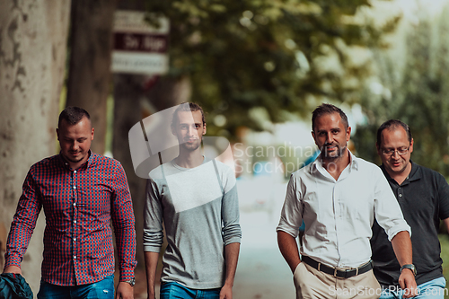 Image of After a productive day at work, a group of diverse colleagues enjoy a leisurely stroll through a modern and natural urban setting