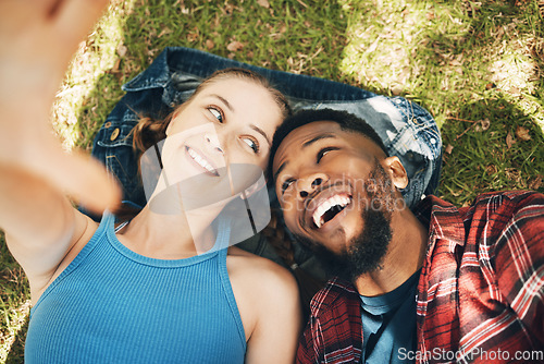 Image of Interracial couple, park selfie and lying on grass with smile, love and happiness to relax on holiday. Black man, woman and profile picture on lawn for social media app with romance, above and care