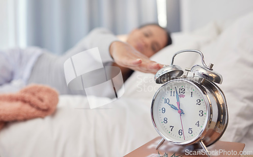 Image of Woman, bed and alarm clock with snooze, sleeping and tired in morning with blurred background in home. Bedroom, watch and wake up time after sleep, rest and relax with burnout, apartment or house