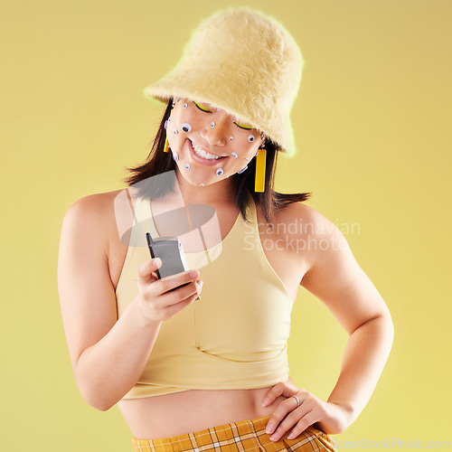 Image of Asian woman, texting and studio with beauty, fashion and eyes sticker art on face with smile for social media. Happy gen z model, 90s aesthetic and phone for communication, chat or app with happiness