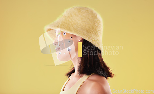 Image of Beauty, makeup and woman with googly eyes in studio for weird, trendy and aesthetic on yellow background. Face, sticker and asian girl model with fun, weird and abstract expression while isolated