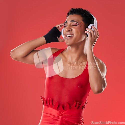 Image of Dance, music and gay man with headphones isolated on a red background in a studio. Freedom, streaming and dancing lgbt person listening to a podcast, radio and audio on a backdrop for entertainment