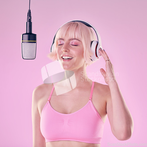 Image of Headphones, microphone and woman singer in a studio recording a song, album or music. Happy, passion and young female artist or musician singing with equipment while isolated by a pink background.