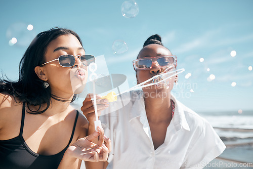 Image of Friends, playing or blowing bubbles by beach, ocean or sea in summer holiday, travel vacation or bonding activity. Women, people or students and soap wand or toy in fun game, freedom or social break