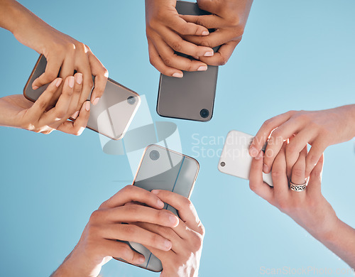 Image of Hands, phone and people networking below on social media or mobile app with blue sky background. Low angle hand of group with smartphone in circle for online share, data sync or team communication