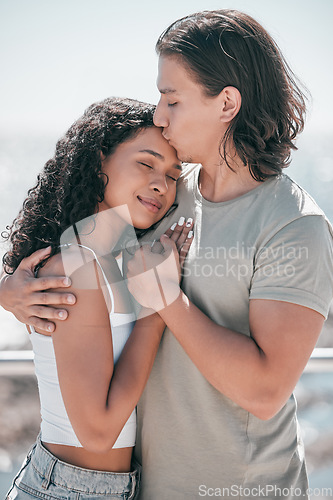 Image of Love, kiss and couple hug at beach, happy and outdoor for travel, romance and bond on blurred background. Forehead, kisses and man embracing woman, sweet and romantic, relation and traveling together