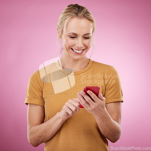 Image of Woman, phone and typing online for communication, social media and chat on pink background. Happy mature model with smartphone in hands for network connection or writing post on mobile app website