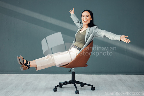 Image of Portrait, chair and celebration of business woman for success, goals or achievements in office. Freedom, carefree and smile of happy Asian female riding on seat, laughing at joke or celebrate targets