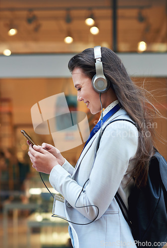 Image of Business woman, phone and smile listening to music in the city for communication, social media or chat. Female walking and typing on smartphone with 5G connection, mobile app and earphones in a town