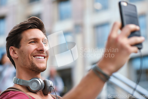 Image of Selfie, man and smile in the city for travel profile picture, social media and influencer streaming. Happiness, vacation and young person online with headphones and memories outdoor on holiday
