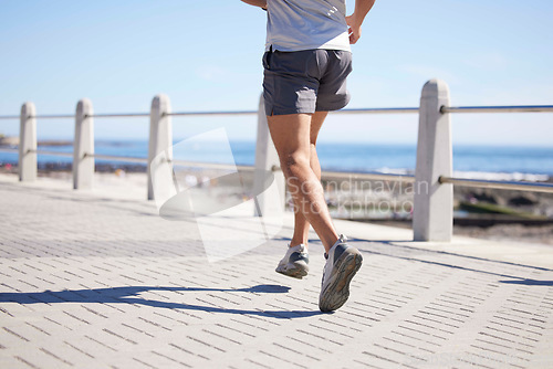 Image of Fitness, sports and legs of man running by ocean for wellness, performance and athlete endurance. Nature, motivation and feet of male runner by sea for exercise, marathon training and cardio workout