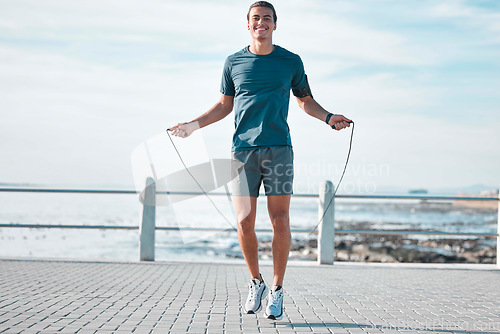 Image of Jump rope, happy and man workout by the beach for his outdoor morning exercise, training and fitness routine. Athlete, cardio and male skipping by the ocean or sea for wellness lifestyle