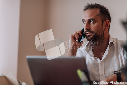 Image of A businessman talking on his smartphone while seated in an office, showcasing his professional demeanor and active communication.