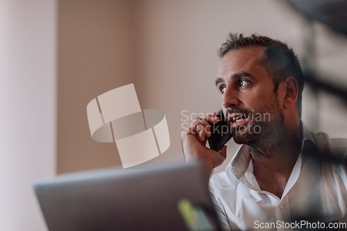 Image of A businessman talking on his smartphone while seated in an office, showcasing his professional demeanor and active communication.