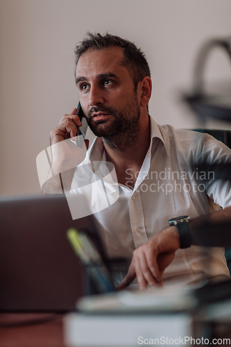 Image of A businessman talking on his smartphone while seated in an office, showcasing his professional demeanor and active communication.
