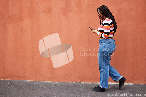 Image of Black woman walking with smartphone in city, outdoor with technology, chat and communication with travel and fashion. Social media, urban street and wall with mockup and 5g, female in Jamaica