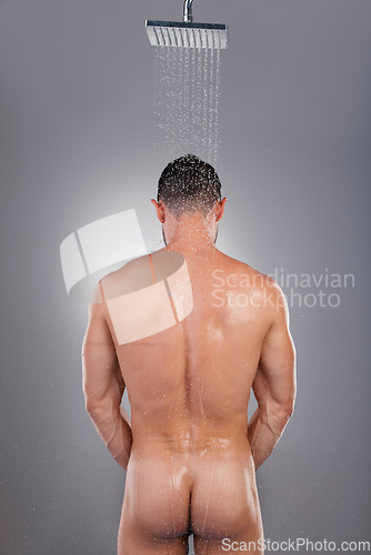 Image of Naked man, shower and back for skincare hygiene or grooming against a gray studio background. Nude male ass washing or cleaning for body care wash under water drops in bathroom routine to cleanliness