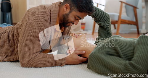Image of Couple, kiss or bonding on floor in house or relax home in love, trust or security. Smile, happy or talking interracial man or woman lying on living room carpet in intimate, romance or support moment