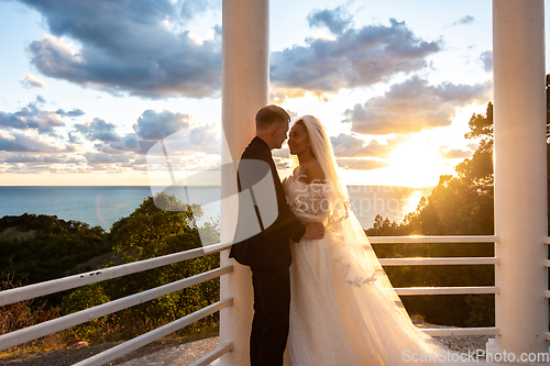 Image of Portrait of newlyweds in a gazebo with columns in the rays of the setting sun