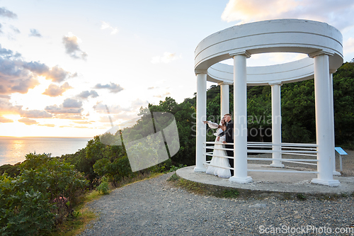 Image of Newlyweds in a gazebo with columns on the seashore in the rays of the setting sun