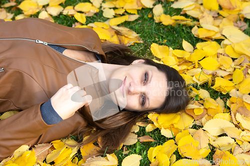 Image of A beautiful girl of Slavic appearance joyfully lies on yellow autumn leaves in the park, close-up