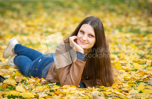 Image of A beautiful girl of Slavic appearance in casual clothes lies on yellow autumn leaves
