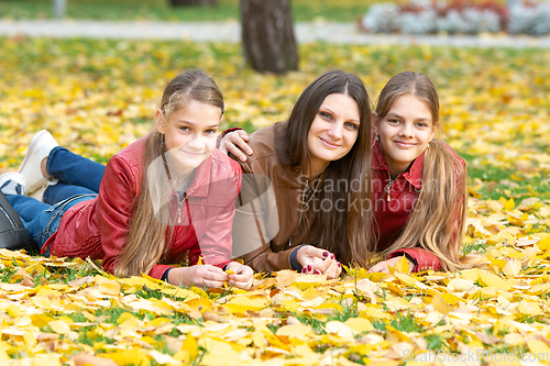 Image of Mom and two daughters of a teenager of Slavic appearance in casual clothes lie on yellow autumn leaves