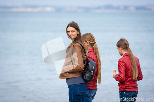 Image of A mother and two daughters are standing on the seashore, the girl turned around and looked into the frame