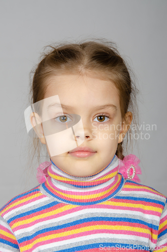 Image of Close-up portrait of a disheveled five-year-old girl wearing a colored striped sweater on a gray background